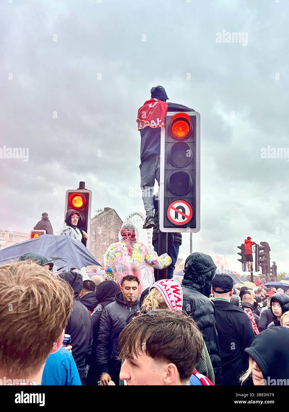 Football fans pack Strand Street Liverpool, climbing traffic lights and street signs in rain gear to watch the team parade, Liverpool, UK, 26 May 2025 - Smartphone Captured Stock Image