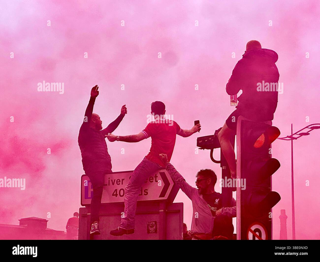 Liverpool fans cheer and sing on top of traffic lights as red flare smoke fills the air during the parade, Strand Street, Liverpool, UK. 26 May 2025. - Smartphone Captured Stock Image