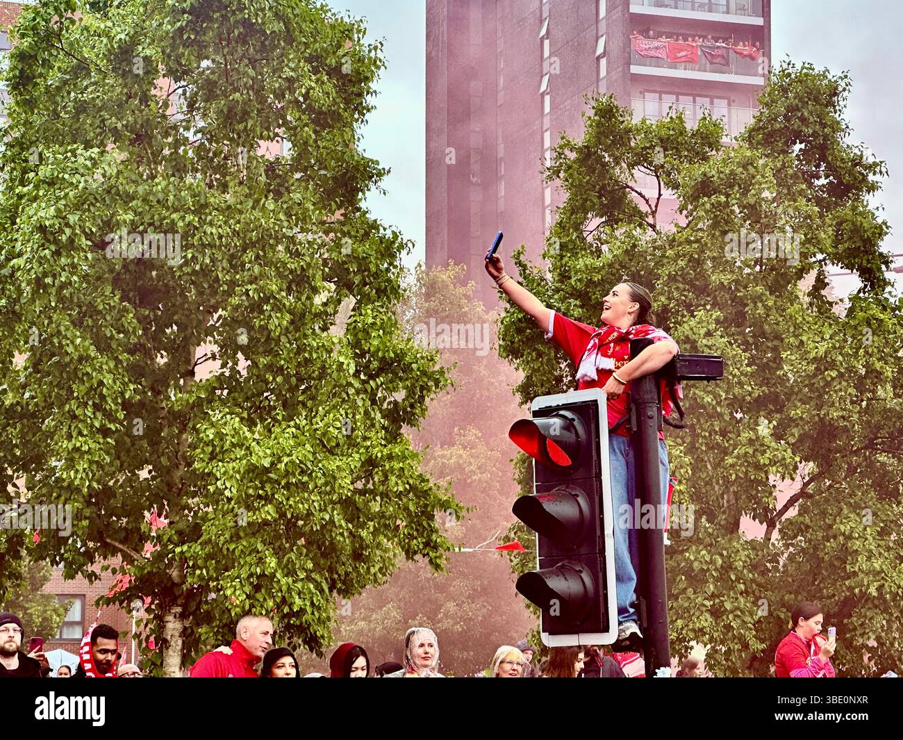 A woman smiles and takes a selfie atop traffic lights during Liverpool’s victory parade on Strand Street, Liverpool, UK. May 26 2025. - Smartphone Captured Stock Image