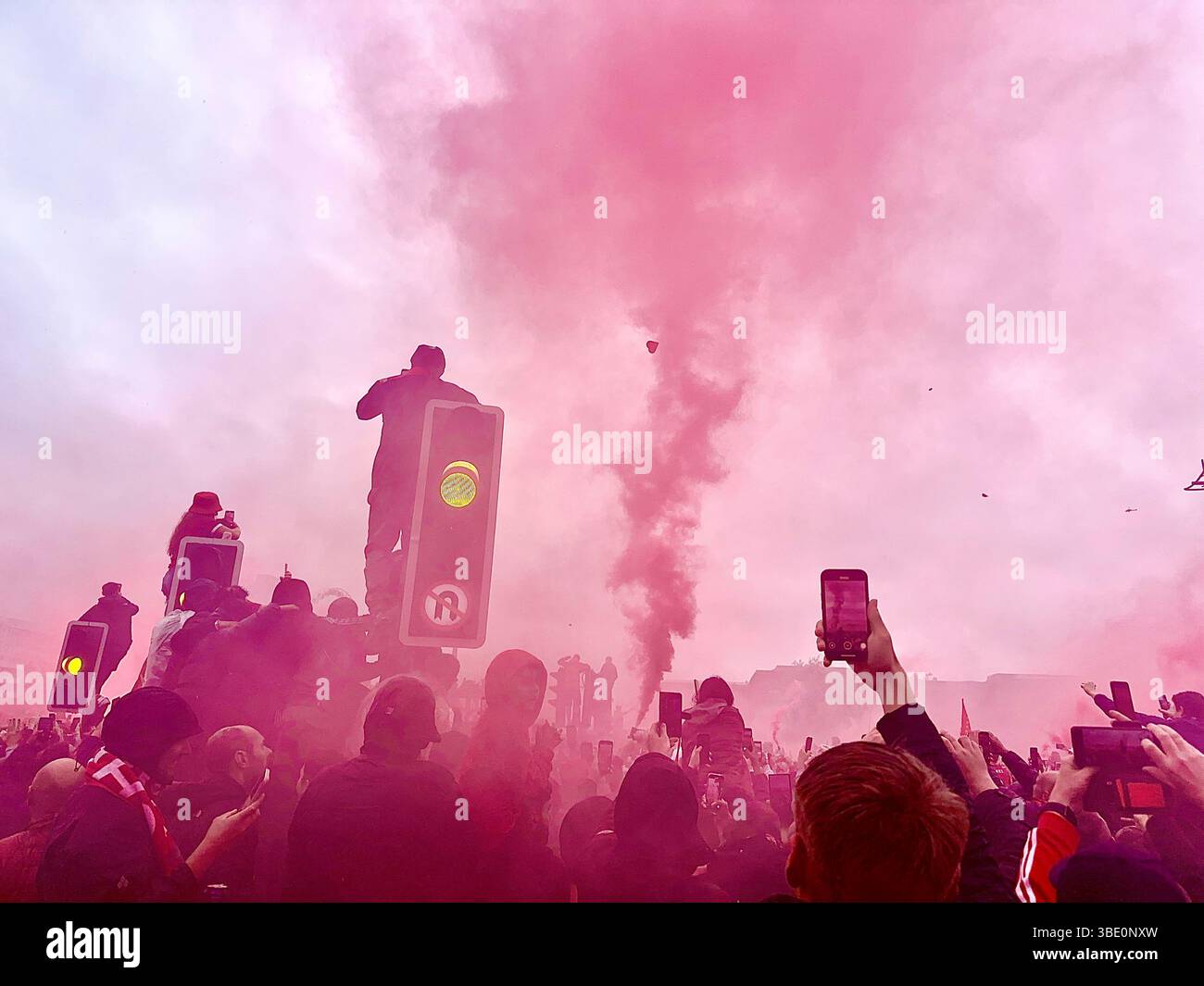 Fans on The Strand climb traffic lights and lift phones in the air through red smoke to glimpse the trophy. Strand Street, Liverpool, UK. May 26 2025. - Smartphone Captured Stock Image