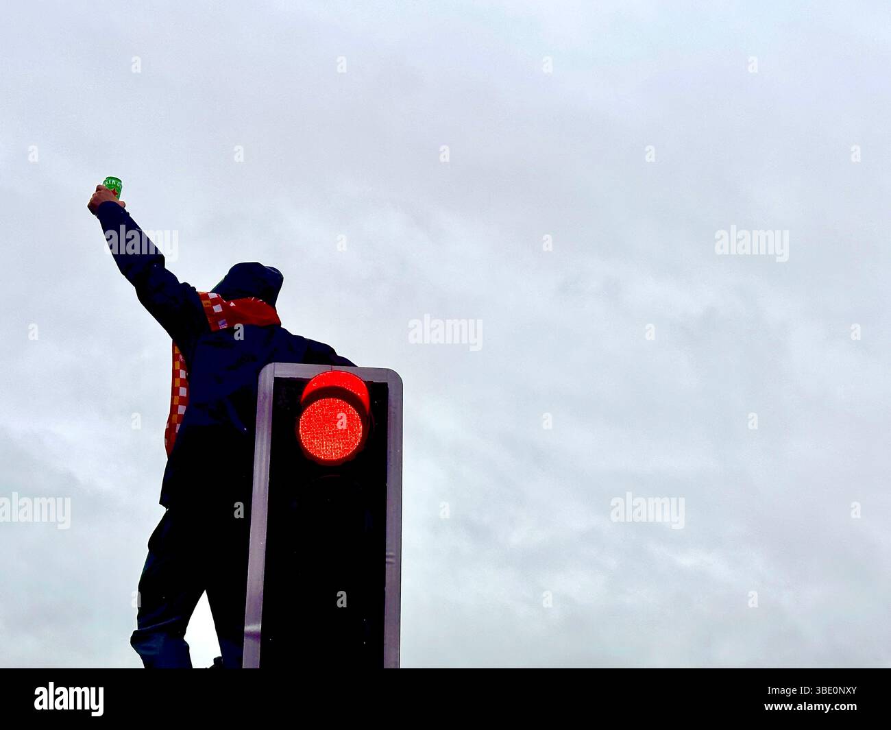 A Liverpool fan raises an arm in triumph while perched on a lamppost during the victory parade. Strand Street, Liverpool, UK. 26 May 2025. - Smartphone Captured Stock Image