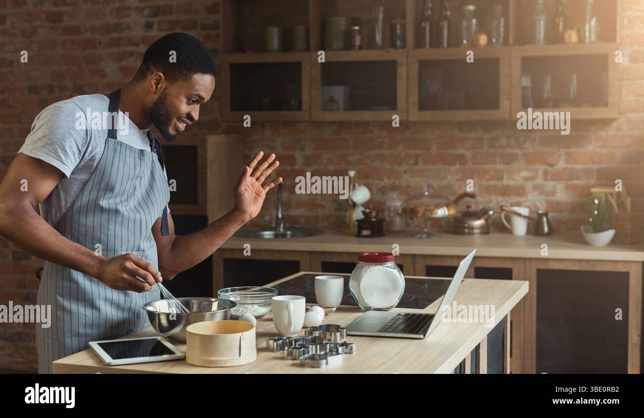 Black man baking pastry and using laptop in kitchen Stock Photo