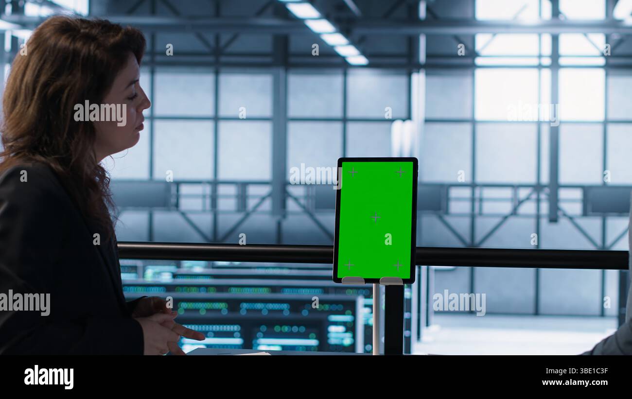 Programmers in data center brainstorming, using mockup tablet, observing equipment analytics. Server hub IT coworkers use isolated screen device, adjusting system parameters, camera A Stock Photo