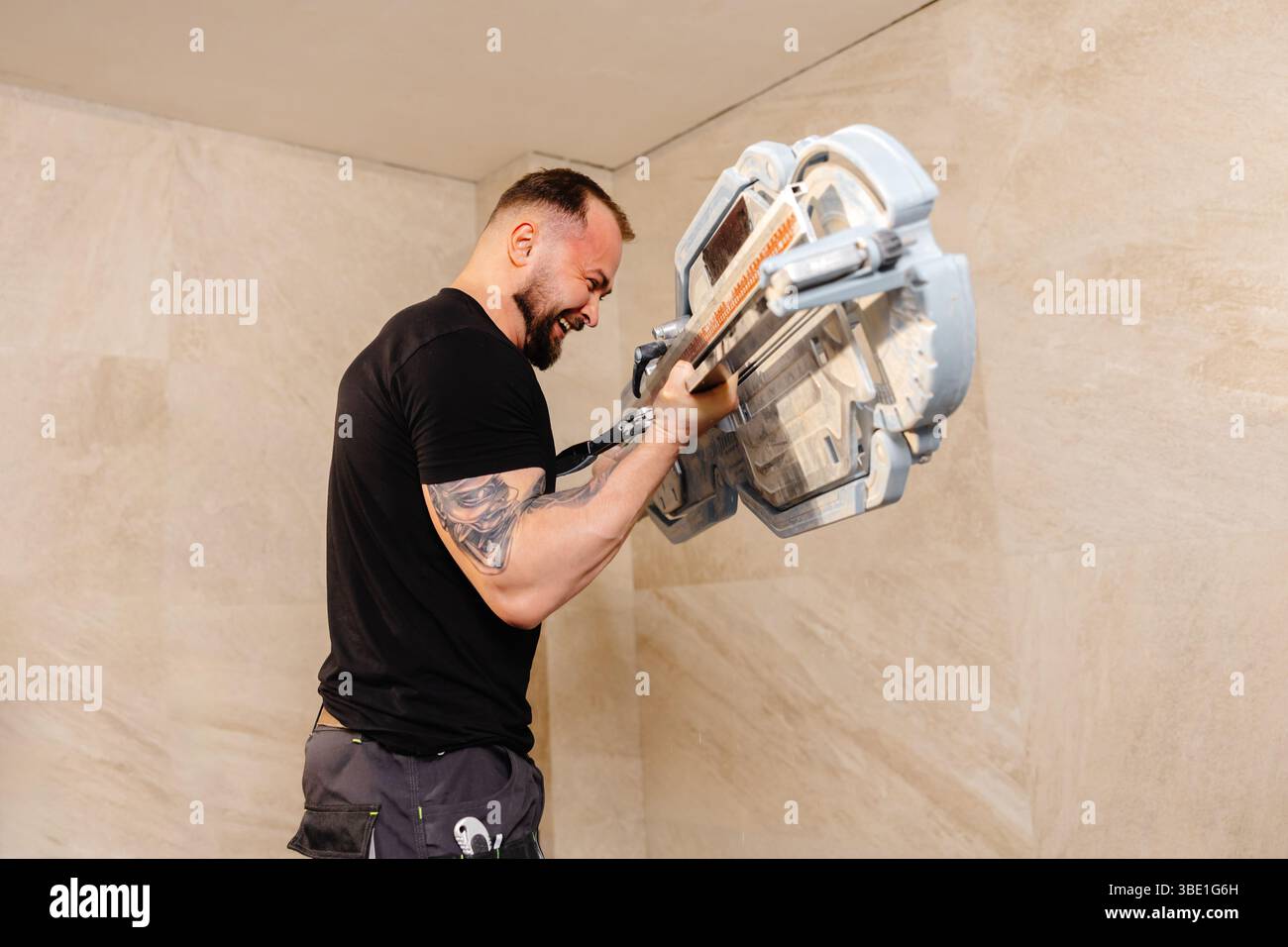 Professional tiler skillfully installing large format tiles on a wall, utilizing a tile cutter for precise cuts during the renovation process Stock Photo