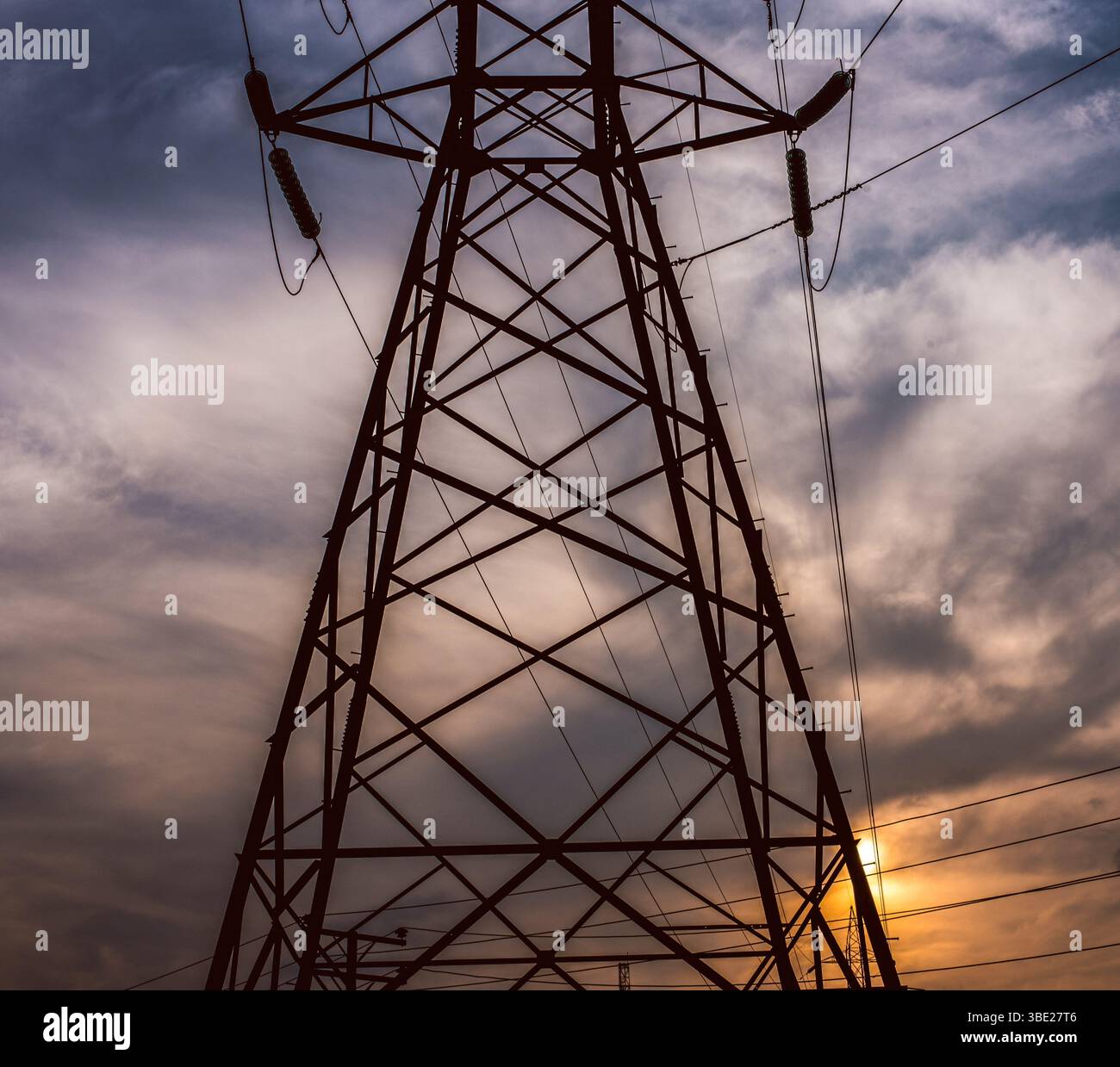 A tall steel high-voltage transmission tower stands against a blue sky ...