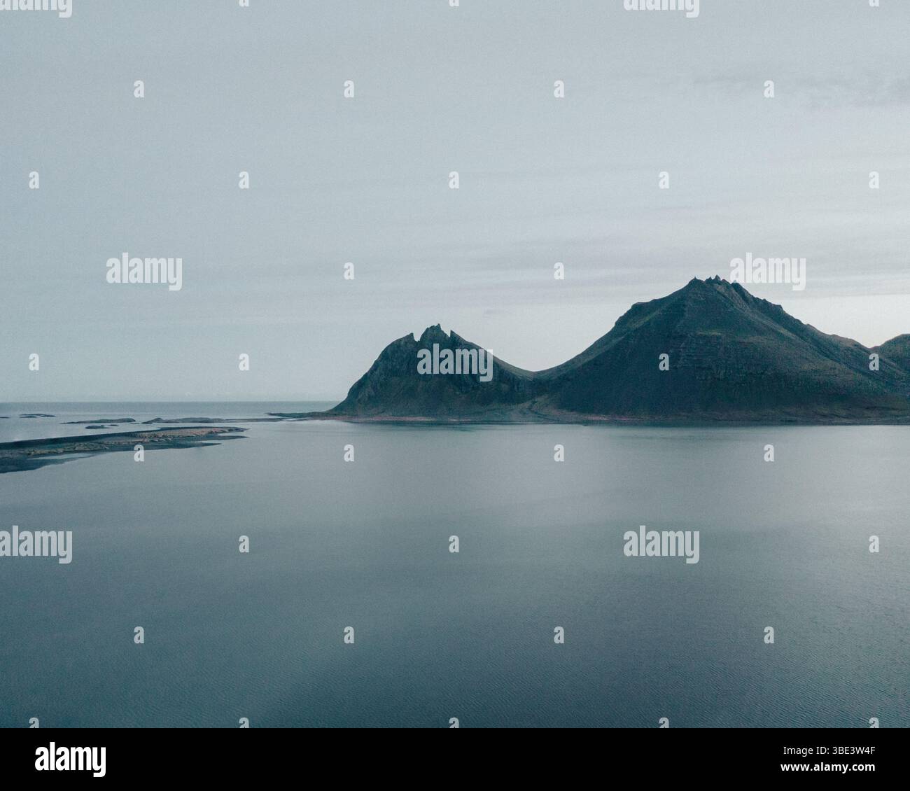 Moody aerial view of Brunnhorn mountain reflected in calm sea, East Iceland. Stock Photo