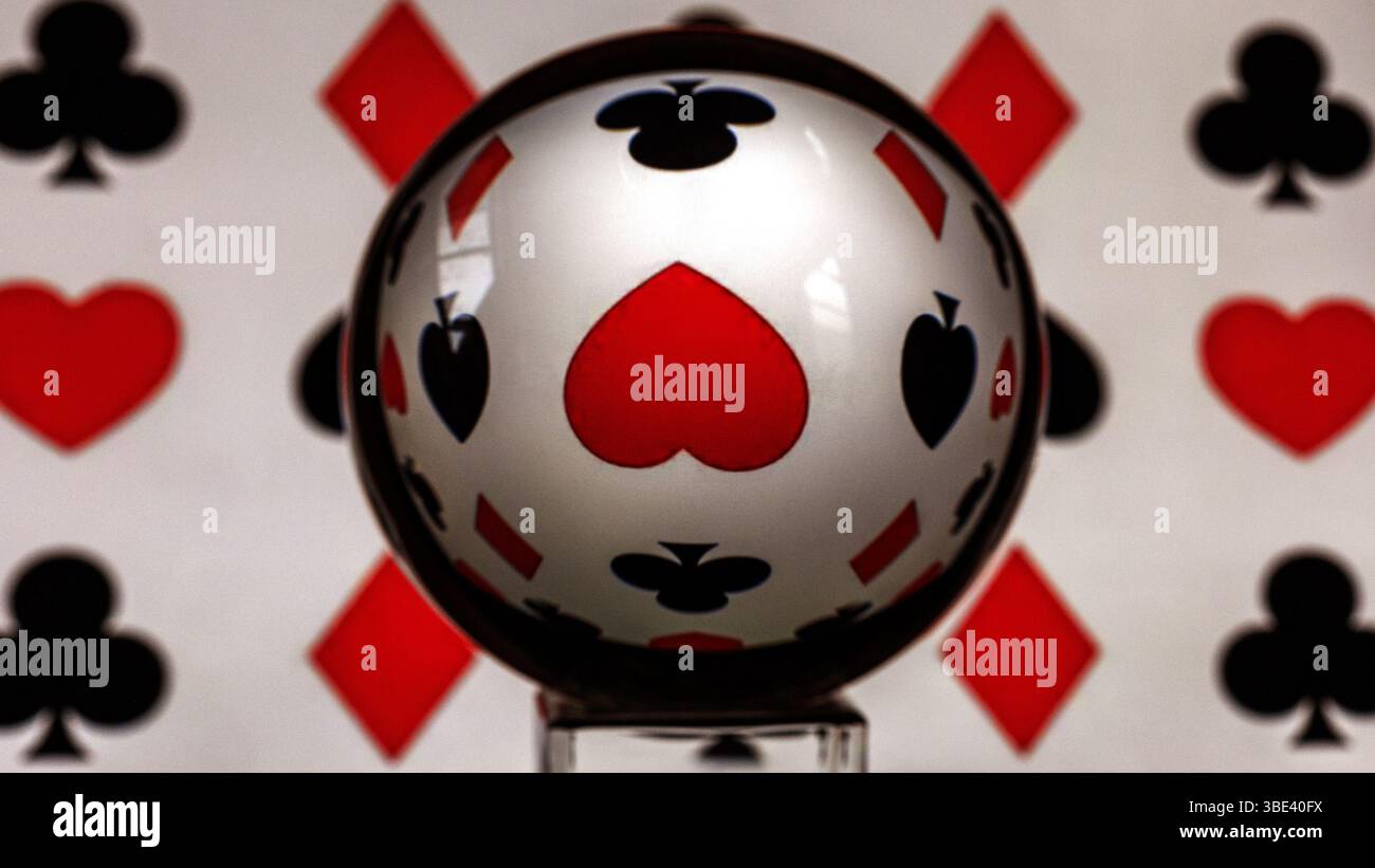 Refracted upside heart as seen through a lens ball surrounded by playing card symbols, diamond, spade and club. - Stock Image