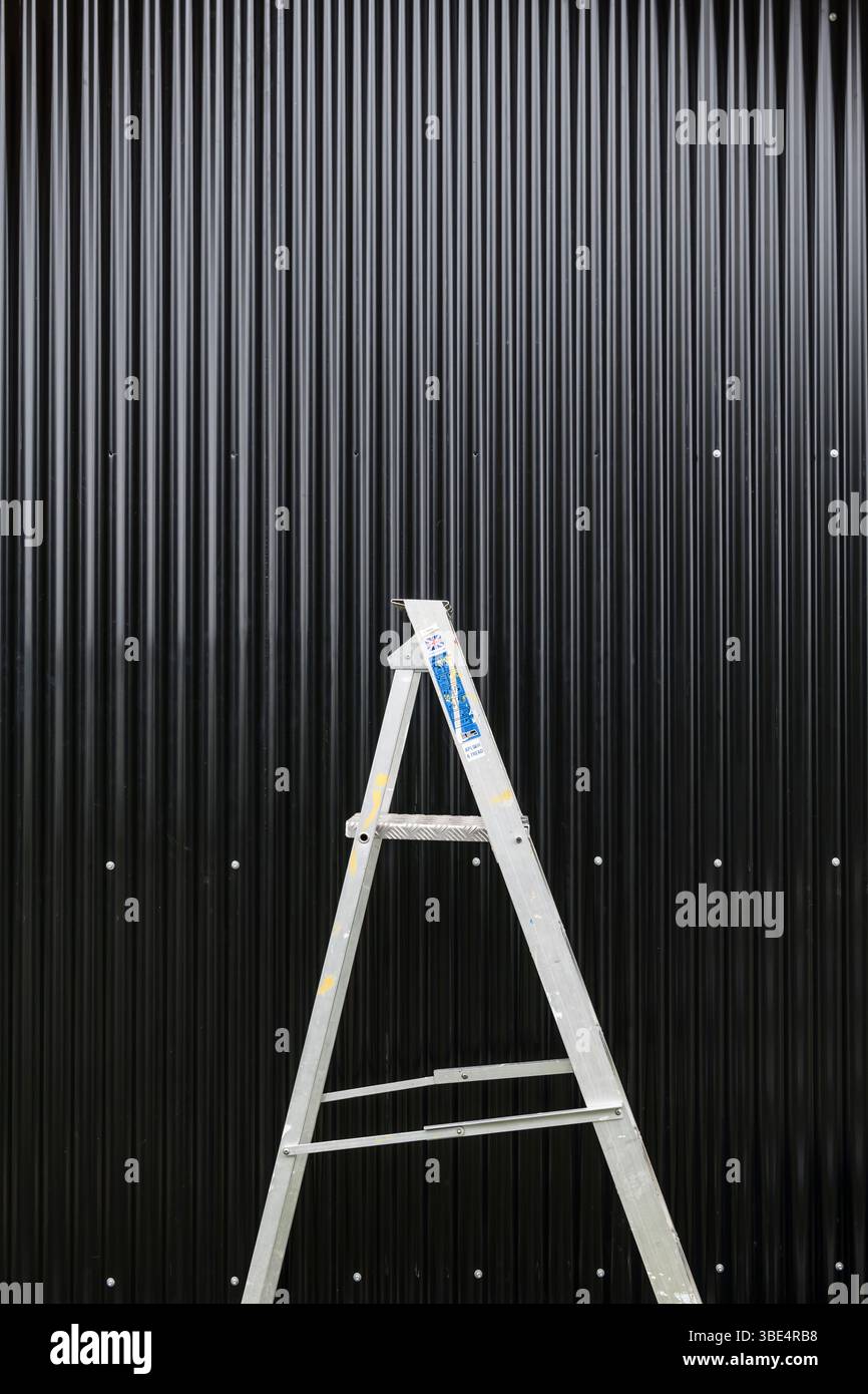 An aluminium stepladder in front of a new black corrugated iron wall Stock Photo