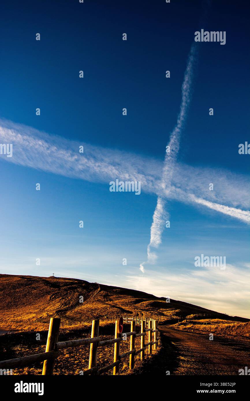 Contrails creating patterns in the blue sky over along a pathway in the ...