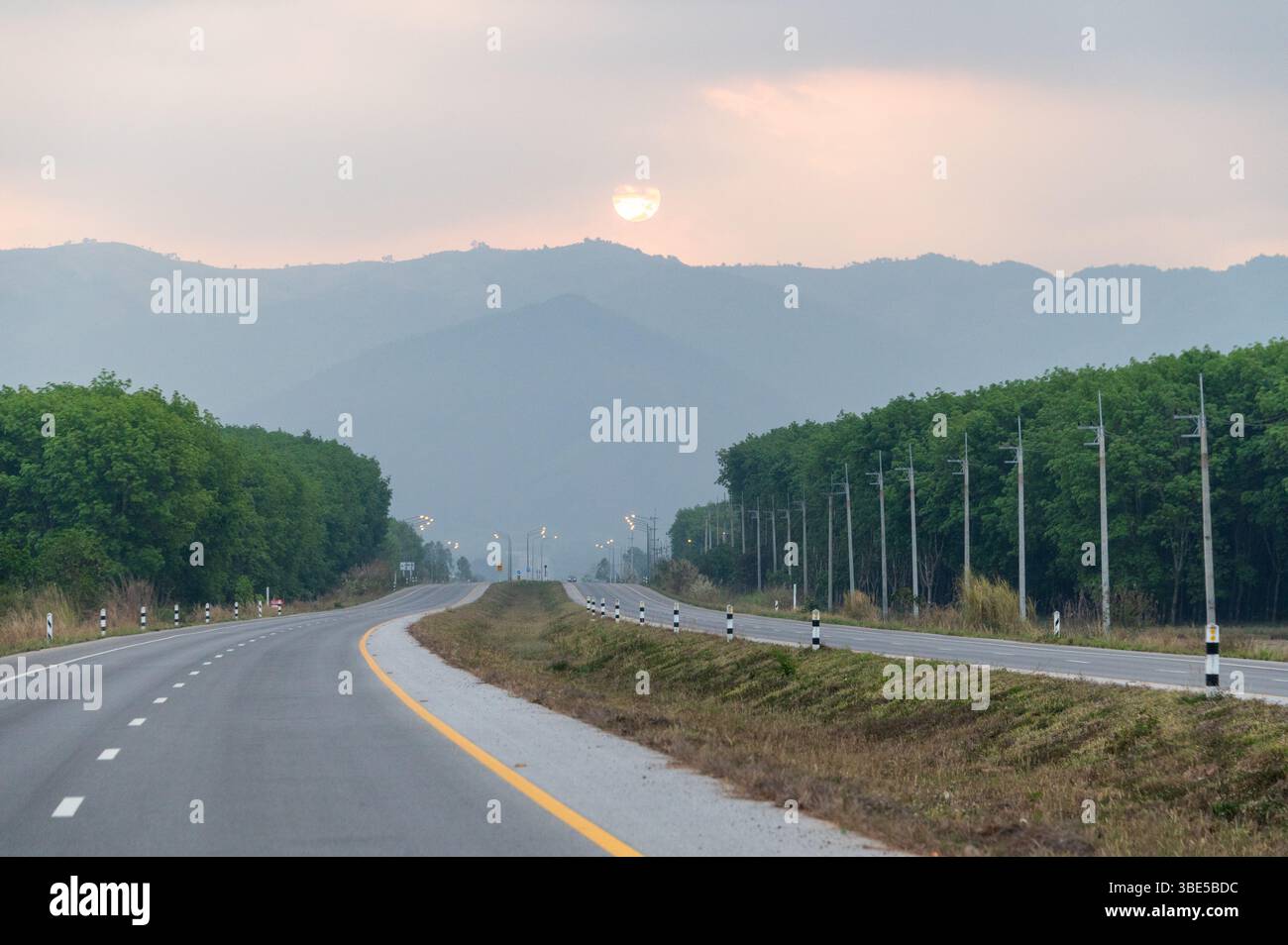 On the almost empty 1020 highway from Chiang Rai to Chiang Khong in northern Thailand as the sun raises above the mountain range on the Thailand/ Myan Stock Photo