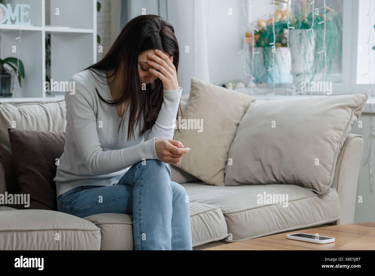 Sad woman sitting on couch with head down and hand covering face Stock ...