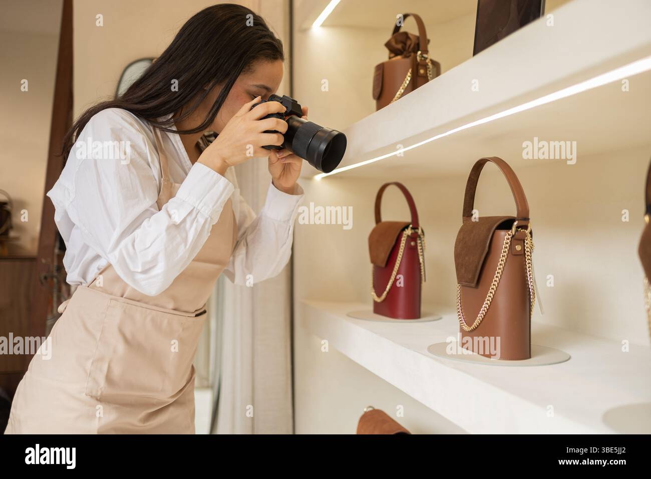 A photographer takes detailed shots of elegant handbags on display in a boutique store. Various leather handbags with chic designs and chain straps ar Stock Photo