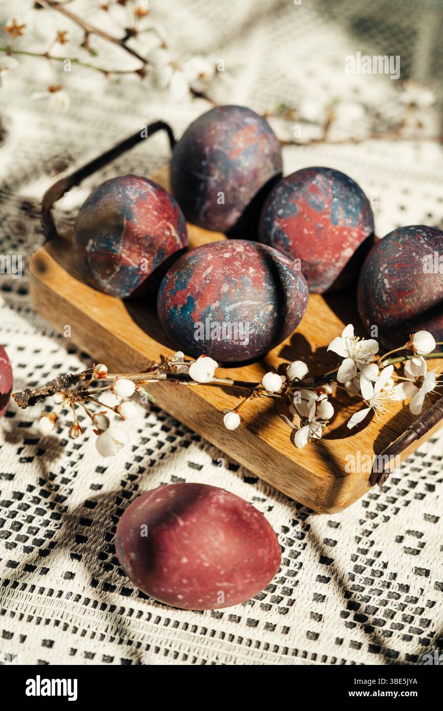 A rustic display of colorful, artistic Easter eggs nestled in a wooden tray adorned with delicate spring blossoms against crochet tablecloth Stock Photo