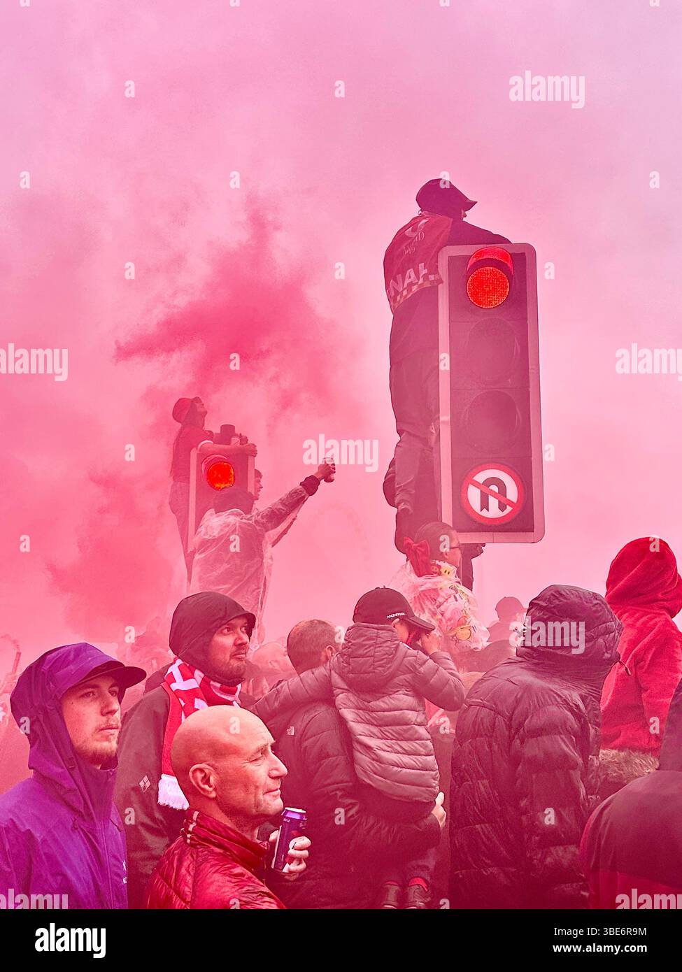 Supporters gather for Liverpool FC’s victory parade on Strand Street, Liverpool, England, 26 May 2025, with fans climbing traffic lights to watch. - Smartphone Captured Stock Image