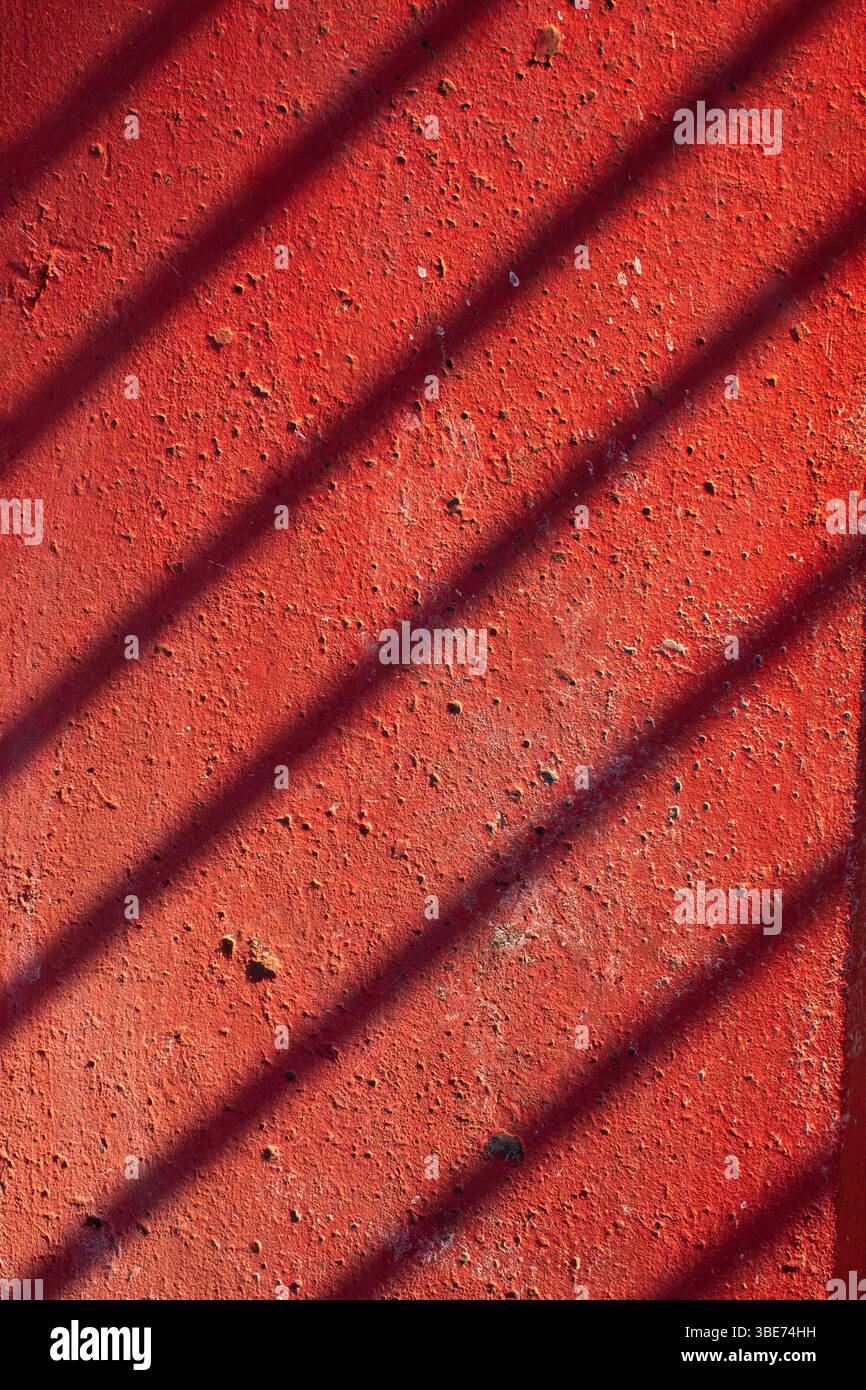 Concrete painted red with a shadow from a fence. Rustic background Stock Photo