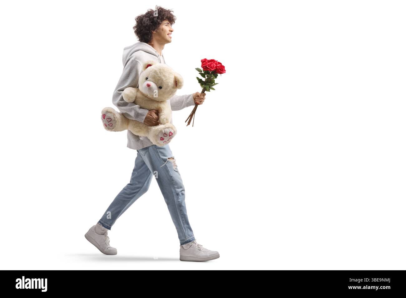 Full length profile shot of a guy carrying a teddy bear and red roses isolated on white background Stock Photo