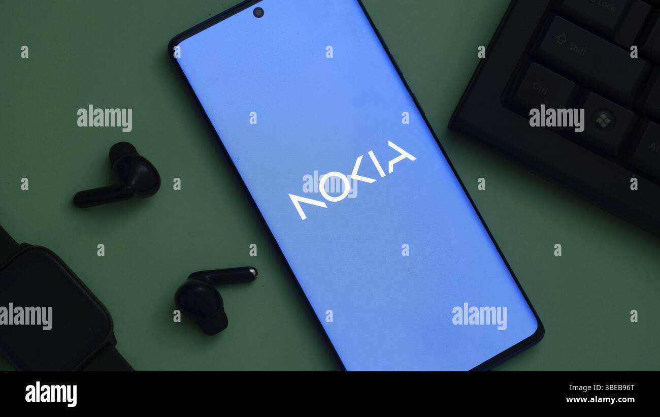 Nokia logo on a smartphone placed on a green surface next to earbuds and a keyboard Stock Photo