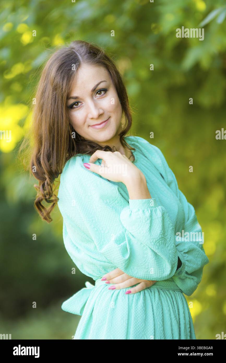 Half-length portrait of a beautiful girl in a dress on a background of green foliage Stock Photo