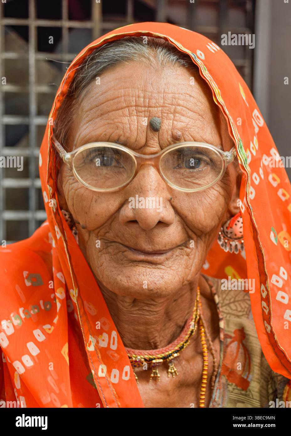 Elderly woman with googles, wrinkles and orange sari looking to camera confident in India. Stock Photo