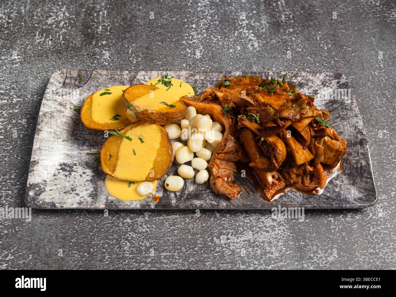Delicious peruvian dish featuring spicy grilled tripe, fried potatoes with huancaína sauce, and cancha corn, served on a marble tray Stock Photo
