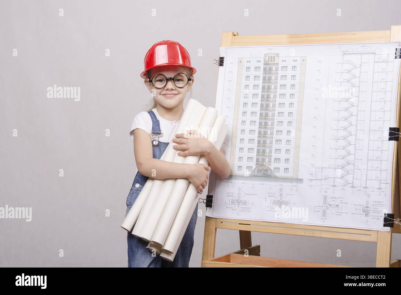 Girl Builder, architect, holding a bunch of drawings, standing at the blackboard with the drawing of the building Stock Photo