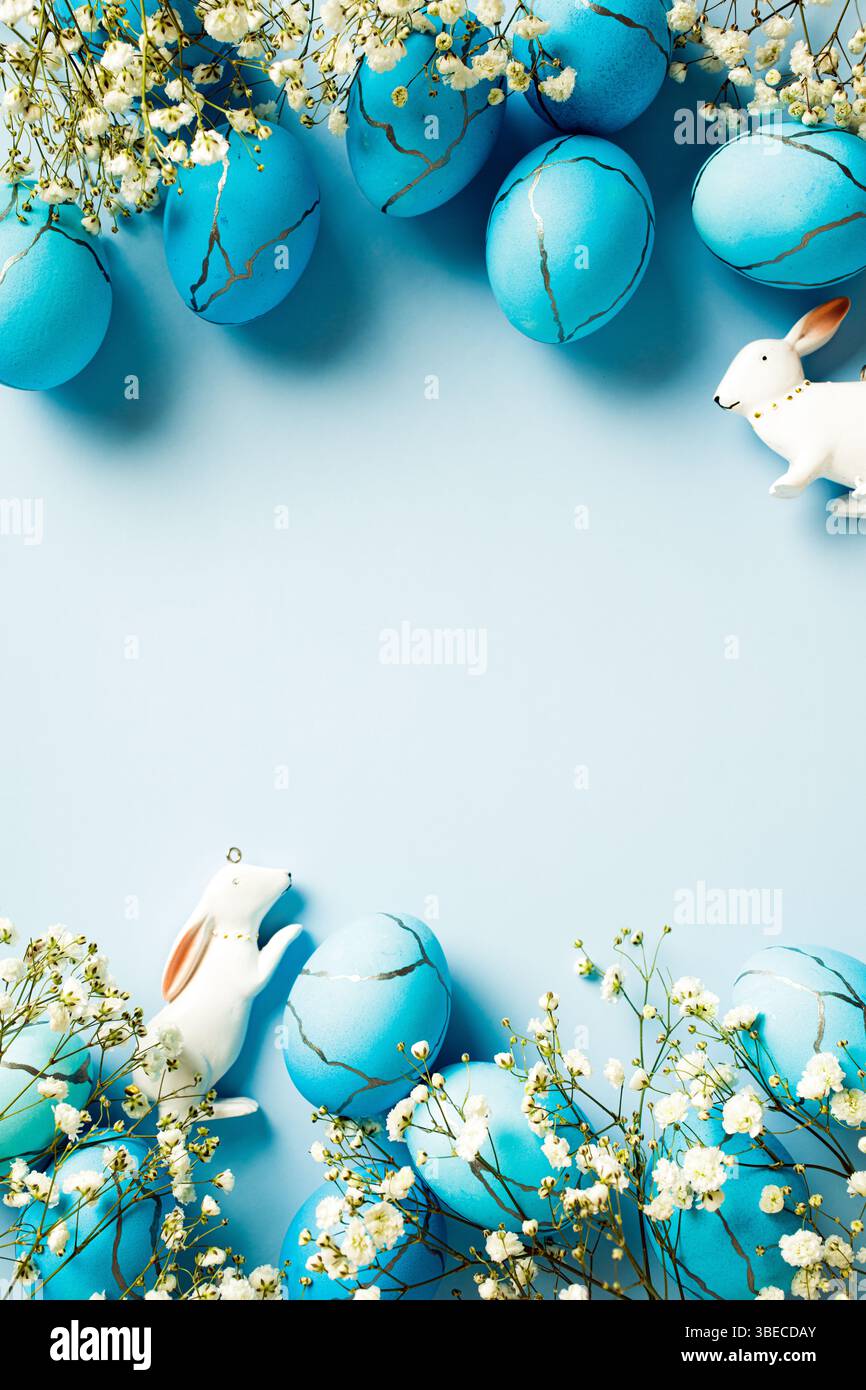 Blue Easter eggs with decorations and flowers on blue background. Vertical flat lay Stock Photo