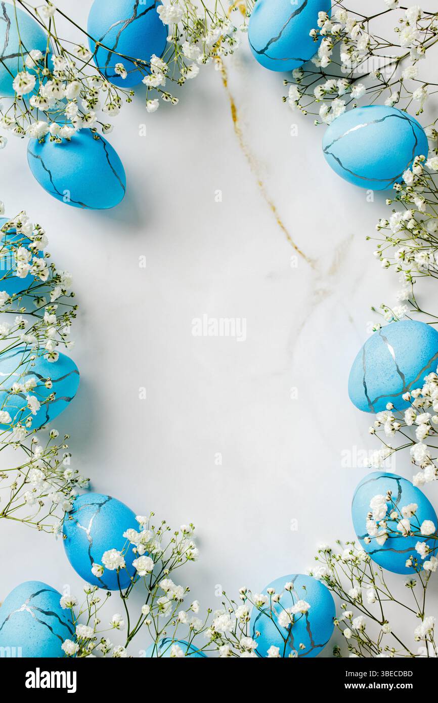 Frame of painted blue Easter eggs with flowers on marble table. Top view vertical Easter background Stock Photo