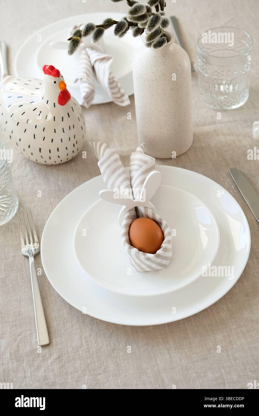 Easter table setting with Easter egg in rabbit napkin on plate and cutlery. Stock Photo