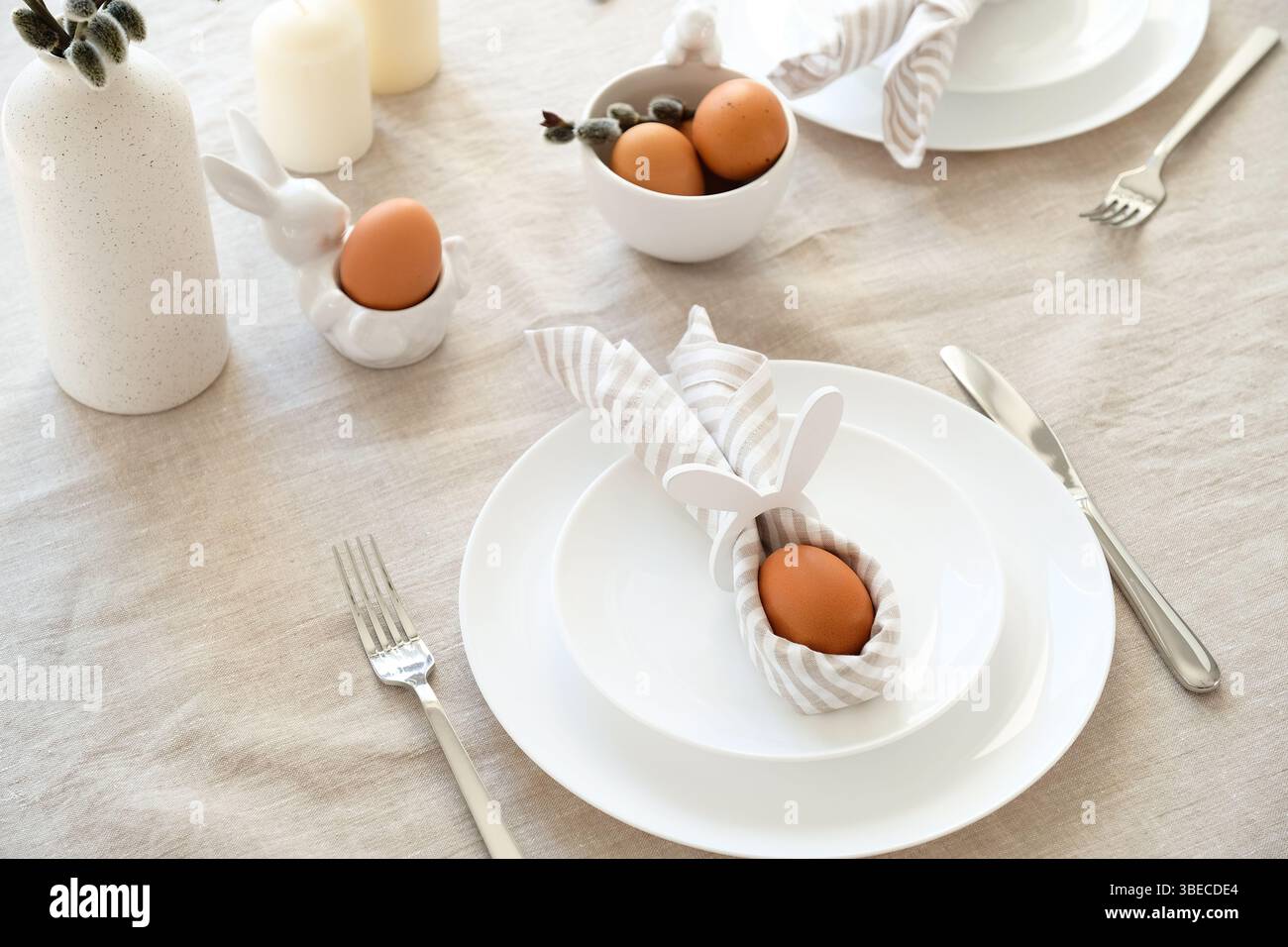 Rabbit Easter egg in napkin on plate. Easter dinner table setting concept. Stock Photo