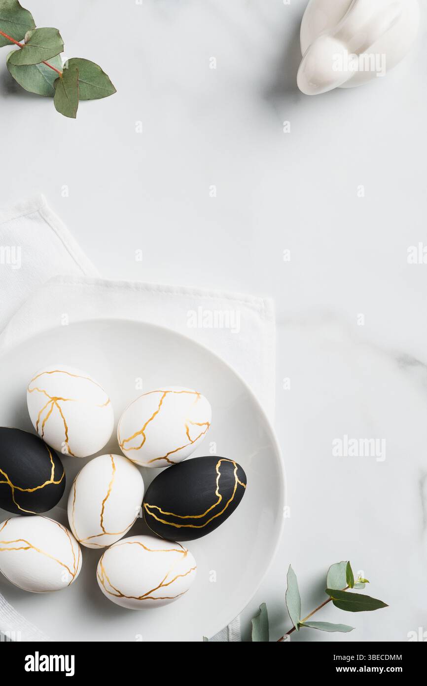 Happy Easter concept. Luxury Easter eggs, bunny rabbit, eucalyptus leaves on marble table. Flat lay, top view, vertical. Stock Photo