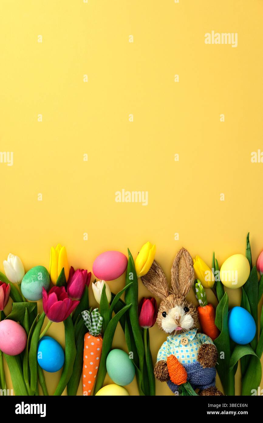 Flat lay composition with painted Easter eggs, tulips, bunny on yellow background Stock Photo