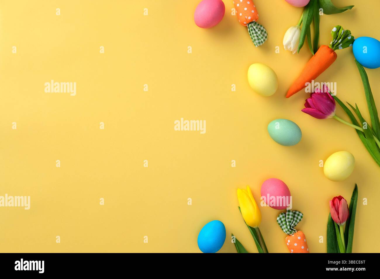 Flat lay colorful Easter eggs and spring flowers on a yellow background. Stock Photo