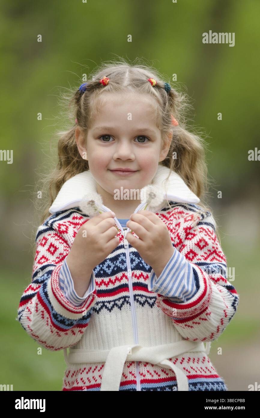 Half-length portrait four-year girl in a jacket with two dandelions in hands Stock Photo