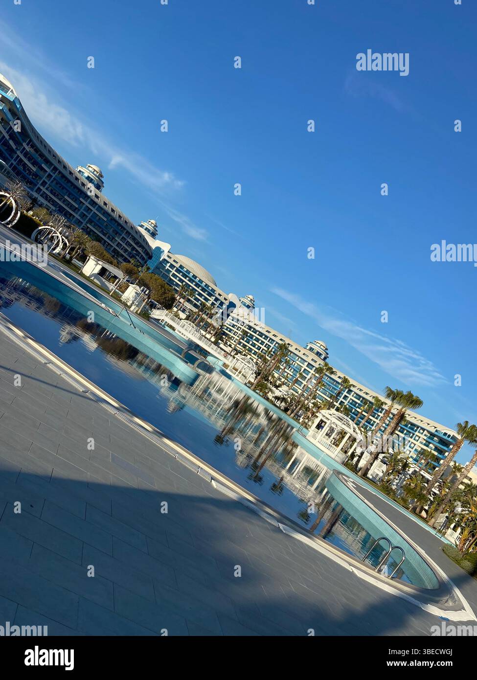 Luxury hotel and outdoor swimming pool under a clear blue sky, surrounded by palm trees and modern architecture in Turkey. - Smartphone Captured Stock Image