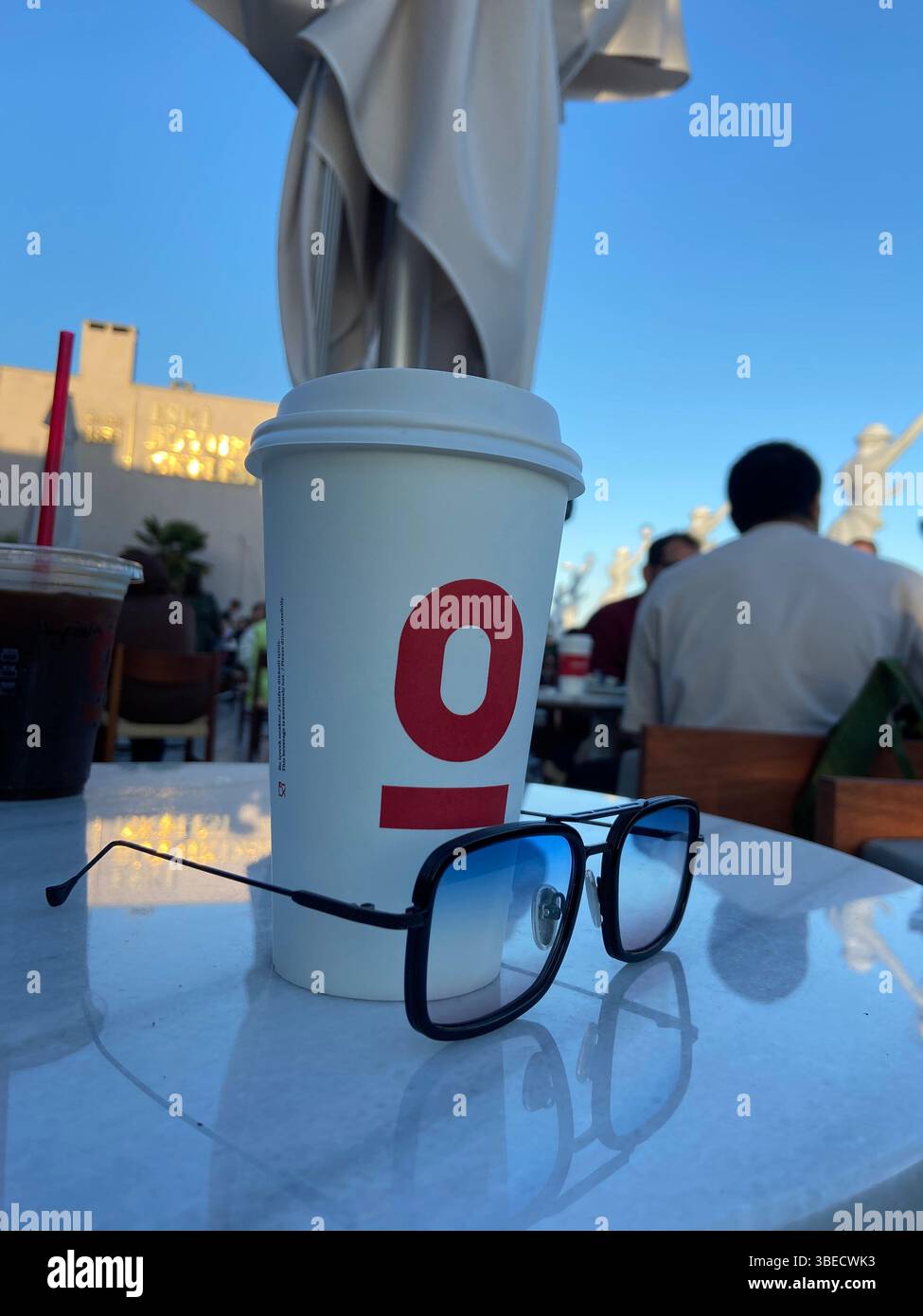 Coffee cup and sunglasses on an outdoor cafe table with a blurred background of people enjoying the sunshine in Istanbul. - Smartphone Captured Stock Image