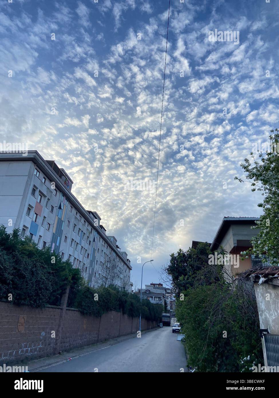 Urban street scene with dramatic cloud formations in the sky, surrounded by residential buildings and greenery in Istanbul. - Smartphone Captured Stock Image