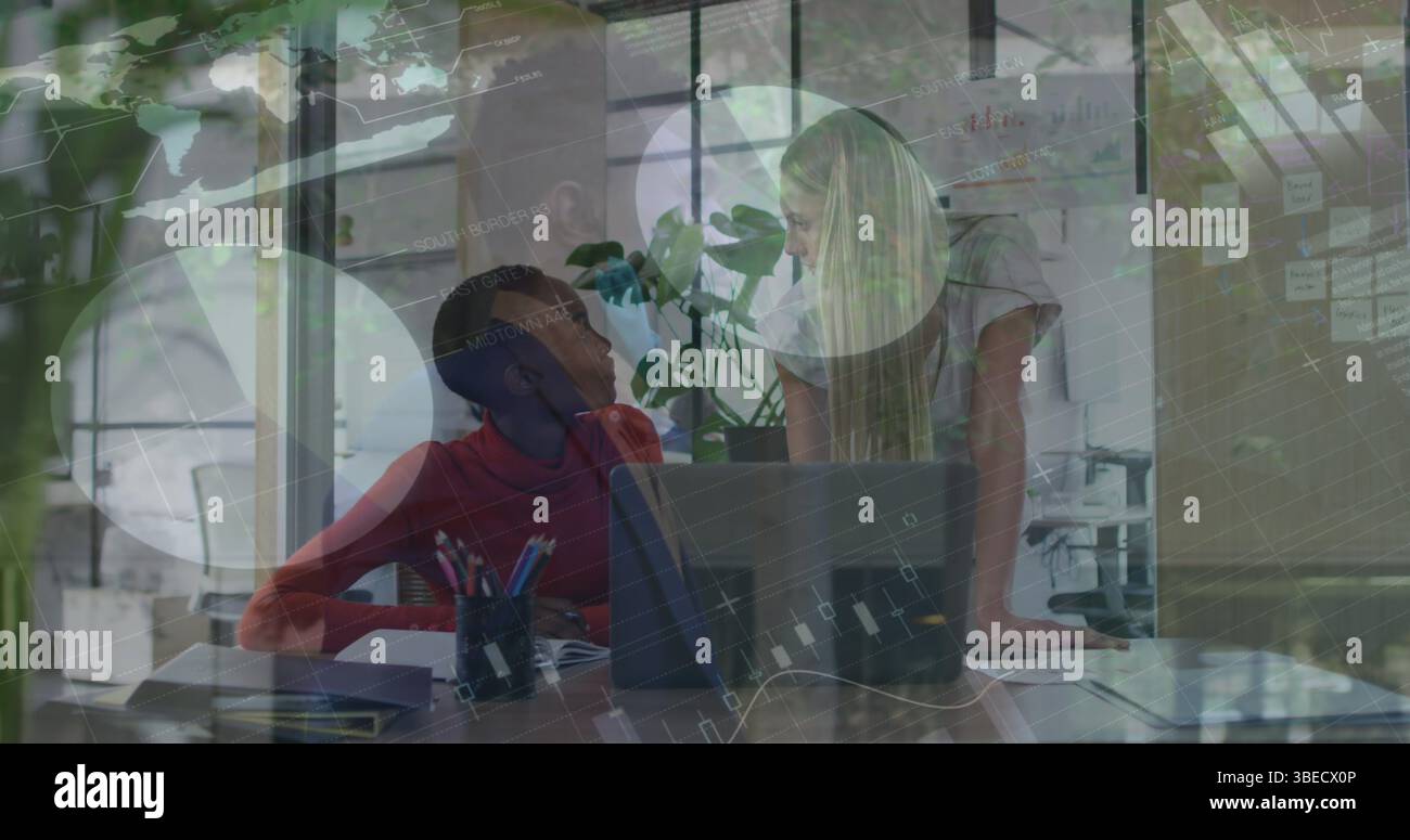 Statistical data processing against two diverse female office colleagues discussing at office Stock Photo