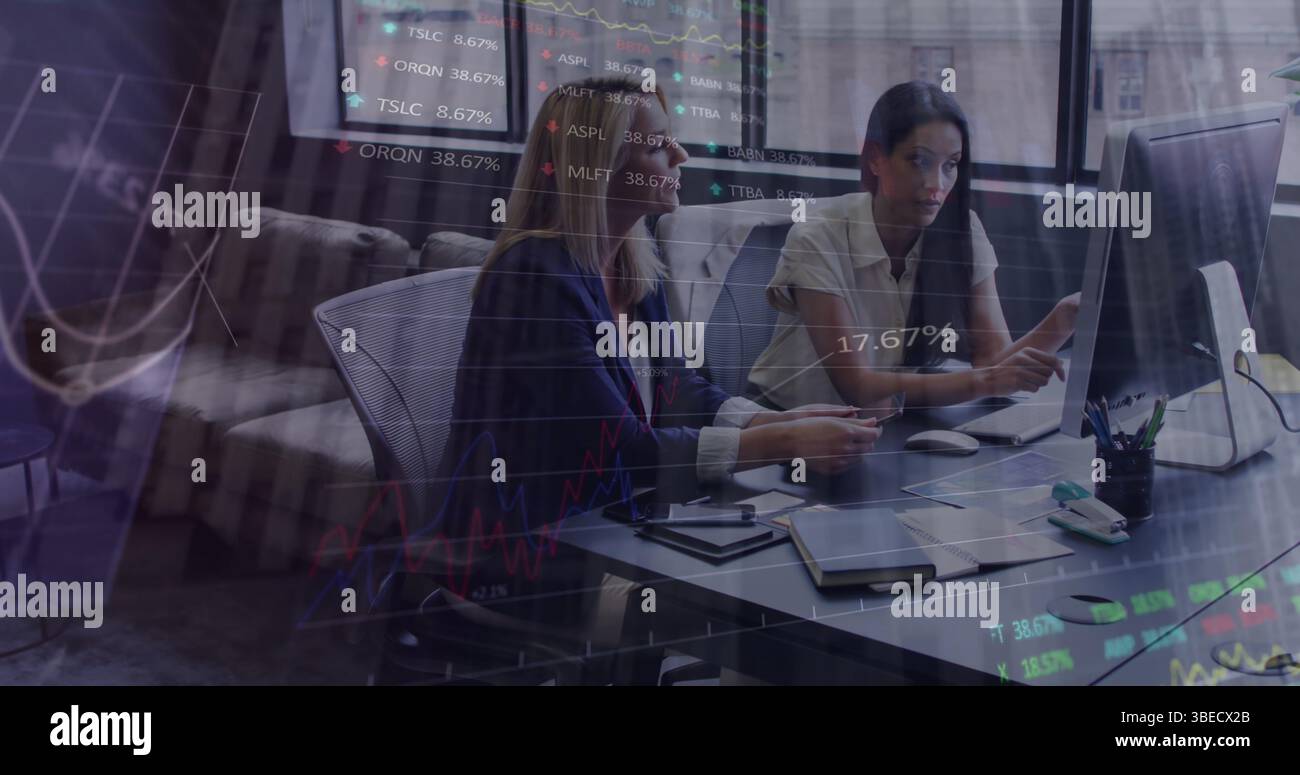 Statistical data processing against two diverse female office colleagues discussing at office Stock Photo