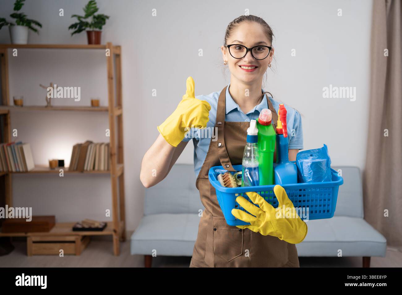 Cleaner woman wearing apron holding cleaning products in basket ...