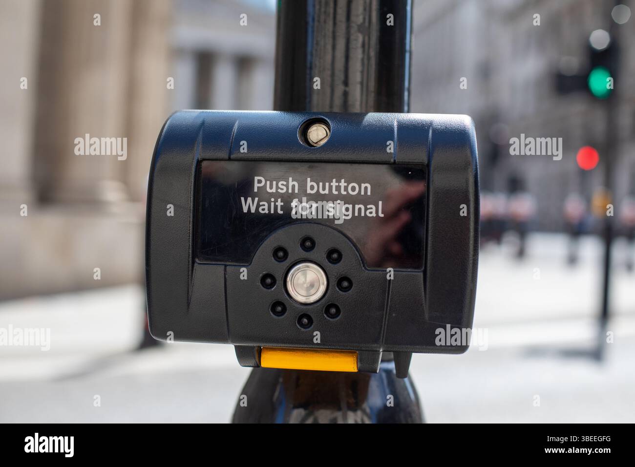 A close-up of a pedestrian crossing button in London. The background shows traffic lights and blurred city architecture. Stock Photo