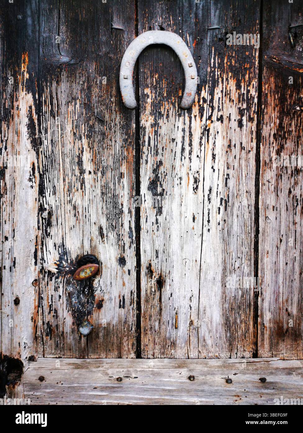 A rustic wooden door features a weathered texture, complete with a vintage horseshoe mounted at the top. Auvergne. France - Smartphone Captured Stock Image