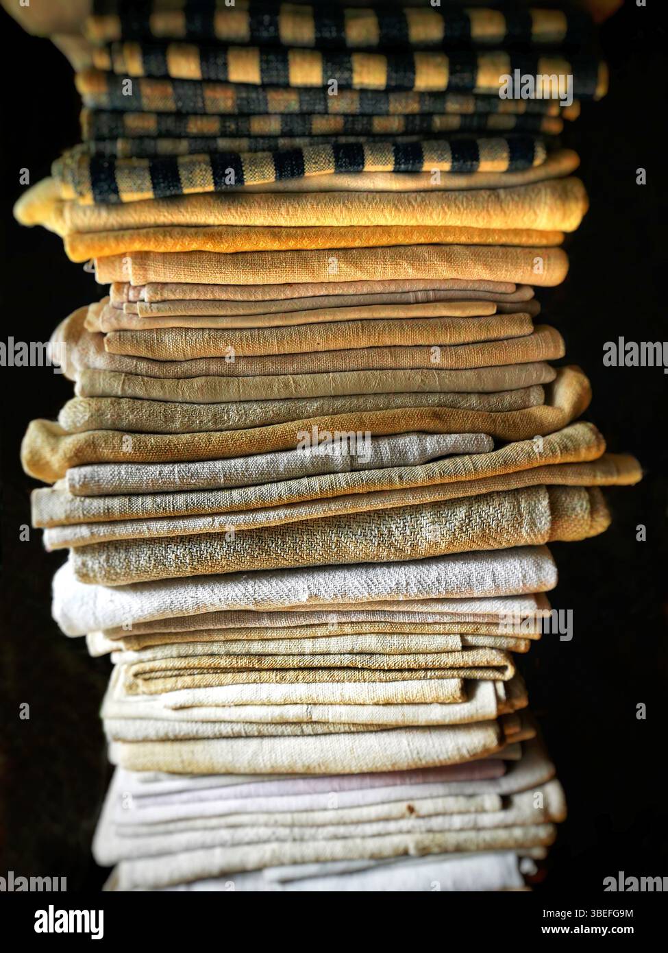 A neat stack of folded textiles in various shades of beige, cream, and a hint of black is illuminated by soft, natural light, enhancing their textures - Smartphone Captured Stock Image