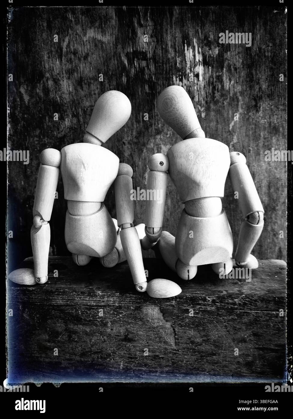 Two wooden figures are positioned closely together, facing away from the viewer. They sit on a rustic wooden surface - Smartphone Captured Stock Image