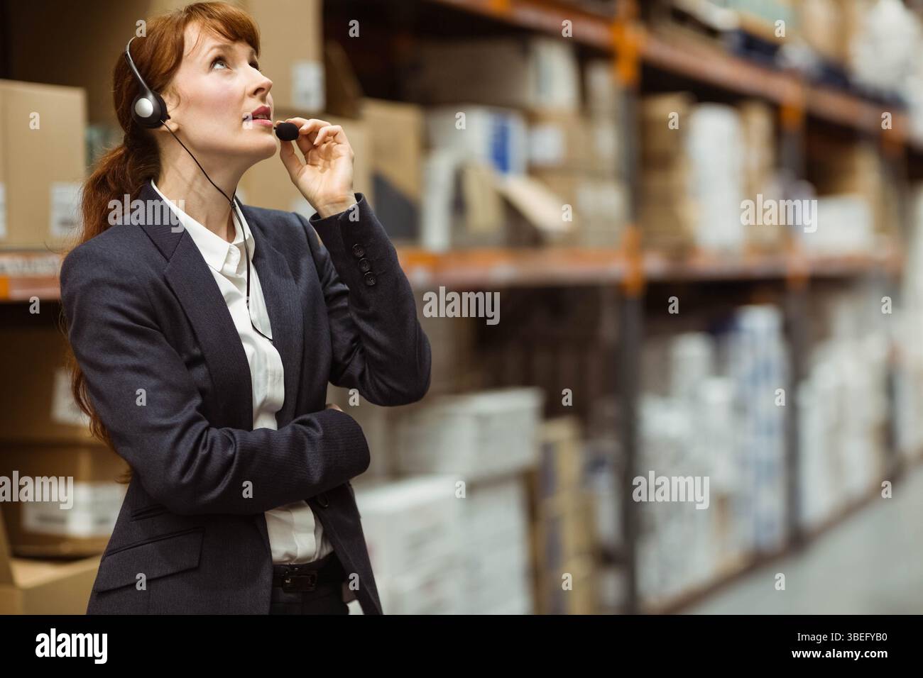 Female supervisor checking boxes on pallets while adjusting headset mic in warehouse, copy space Stock Photo