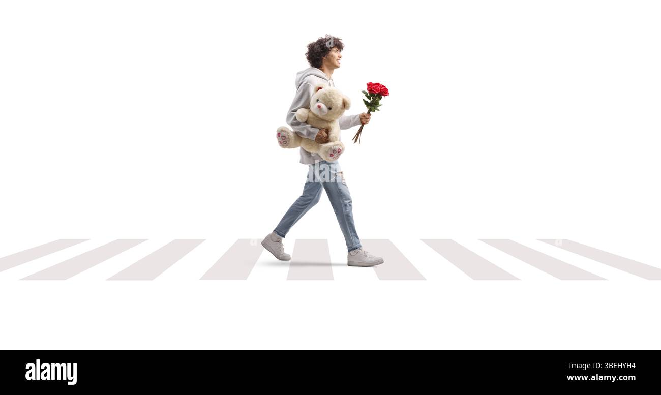 Full length profile shot of a guy crossing a street with a teddy bear and red roses isolated on white background Stock Photo
