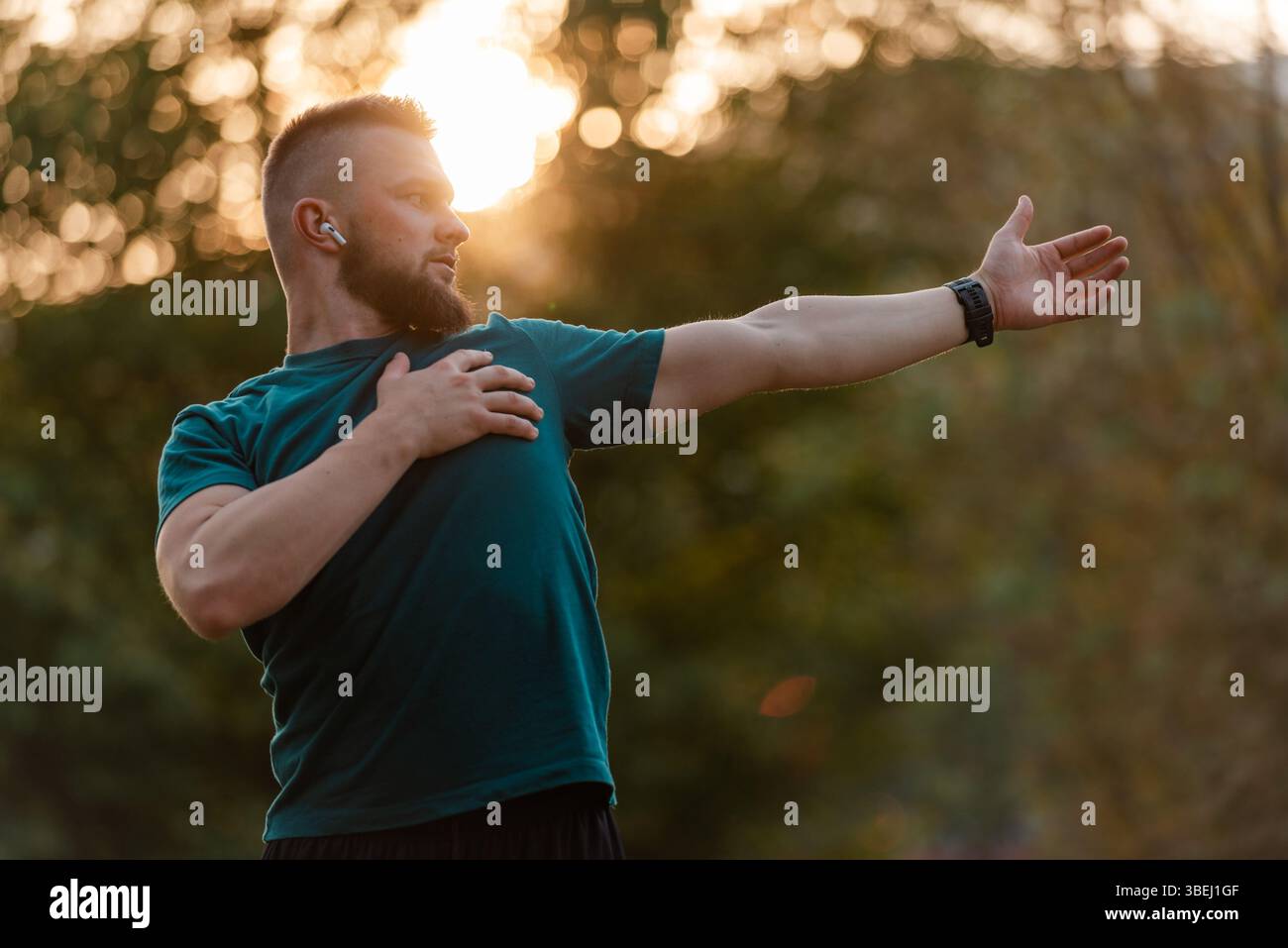 A sporty man listening to music on wireless headphones and doing stretching exercises before running or workout outdoor in the summer park active Stock Photo