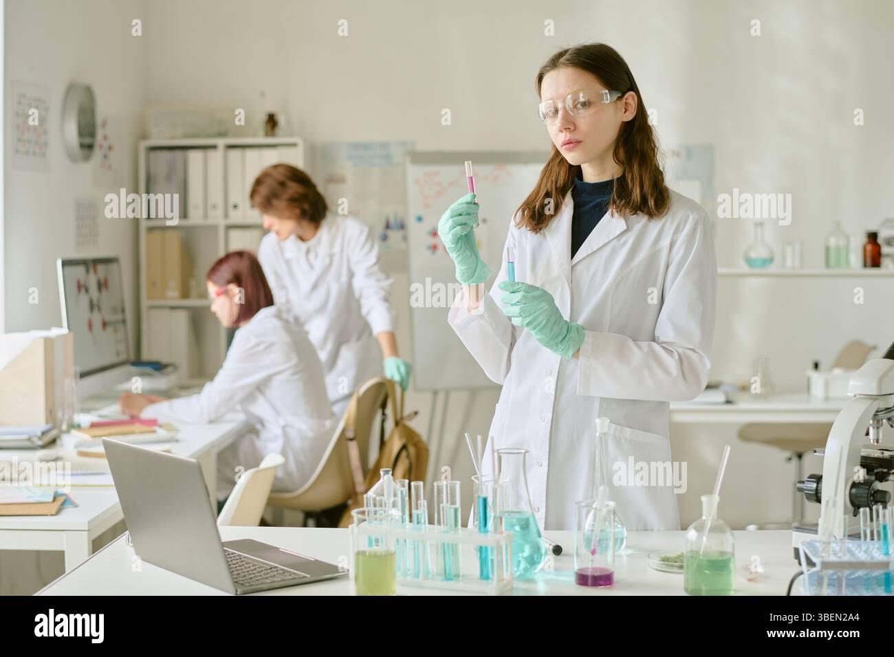 Scientists in lab coats conducting experiments with various chemical substances in modern laboratory environment having lab equipment and devices on b Stock Photo