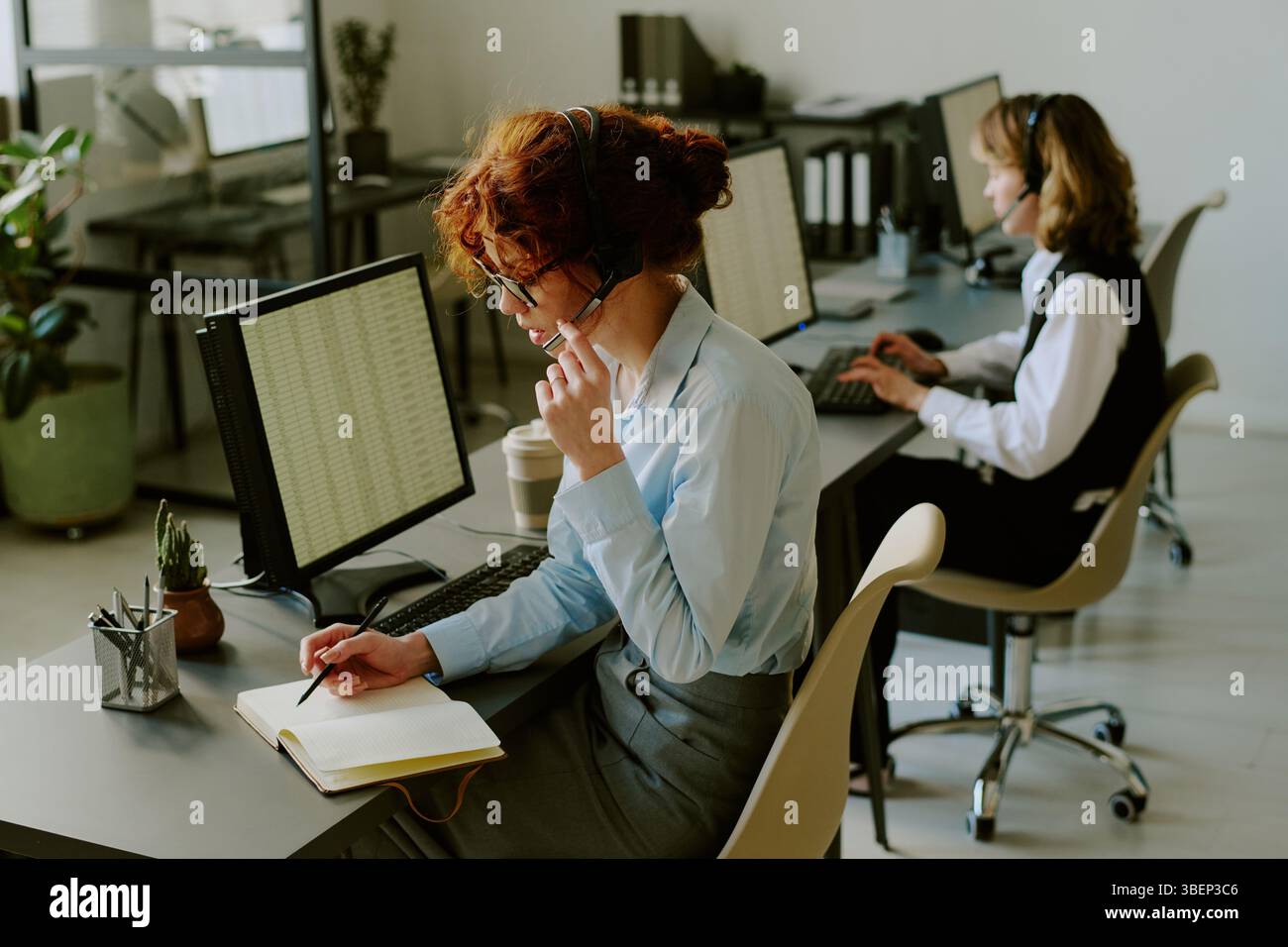 Two office workers focused on tasks at their desks, with one taking ...