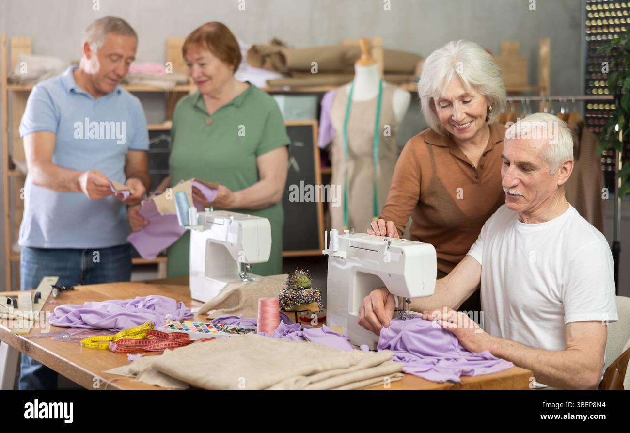 Some people communicate and discuss pattern, while others sew using sewing machine at lesson Stock Photo