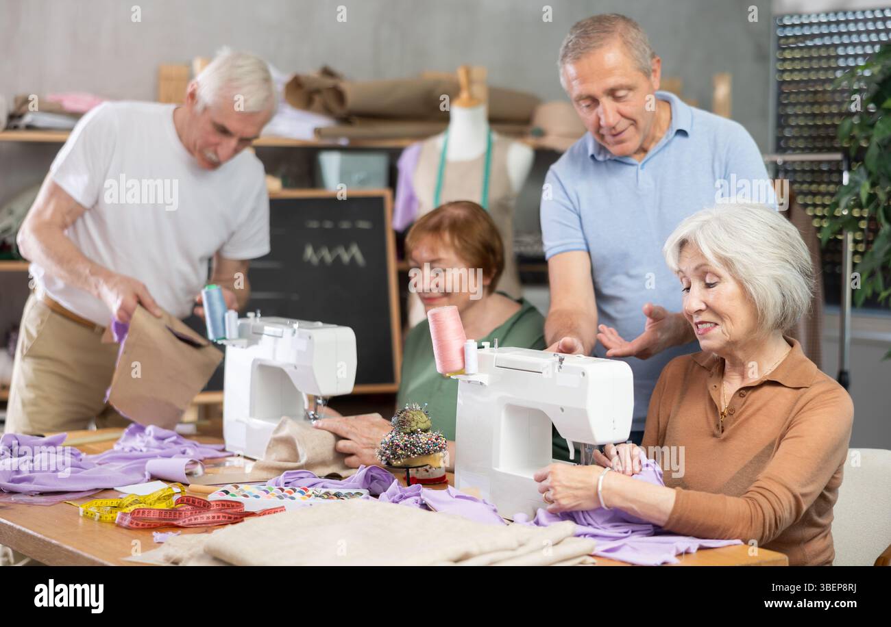 Some people communicate and discuss pattern, while others sew using sewing machine at lesson Stock Photo